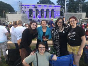 2 faculty members and three graduate students smiling in front of amphitheater for Shakespeare in the Park 