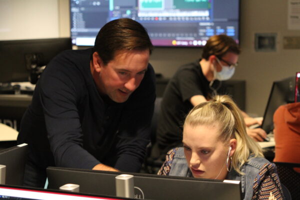 Instructor David Plough assists as student in Podcasting class
