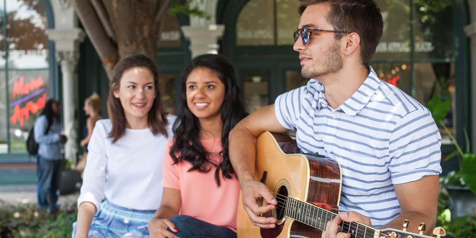 A student plays the guitar while two others listen.