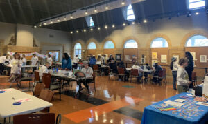 Large room with multiple tables set up as art stations with about 30 people participating in art-making and conversation with one another. 